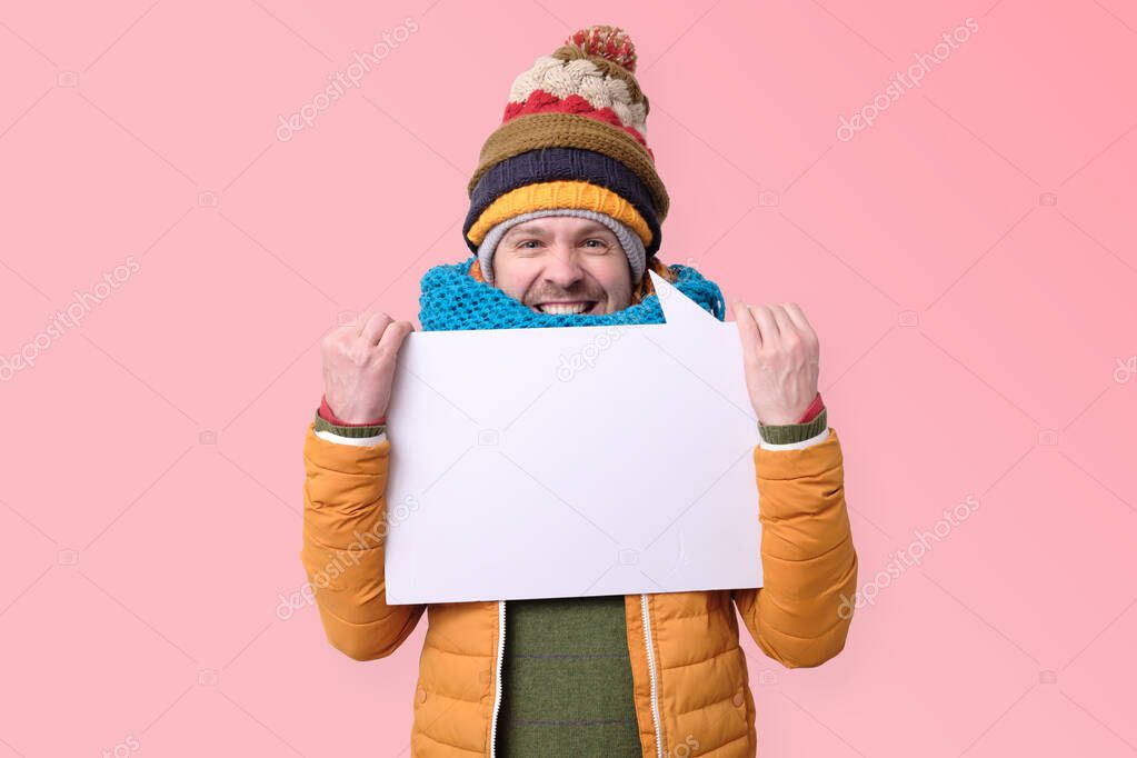 Smiling young man in warm winter hats holding blank sign in hands