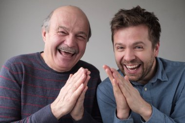Mature father and son smiling mysteriously, clasping hands, scheming something, keeping secret clipart