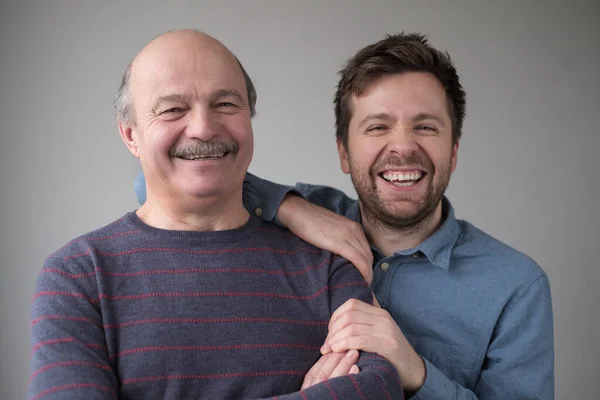 Smilende senior mand med sin voksne søn smilende med positivt humør - Stock-foto