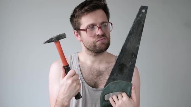 Funny young caucasian man choosing hammer and saw — Stock Video