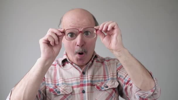 Überraschter gutaussehender Senior schaut durch Brille auf Schockinhalt. — Stockvideo