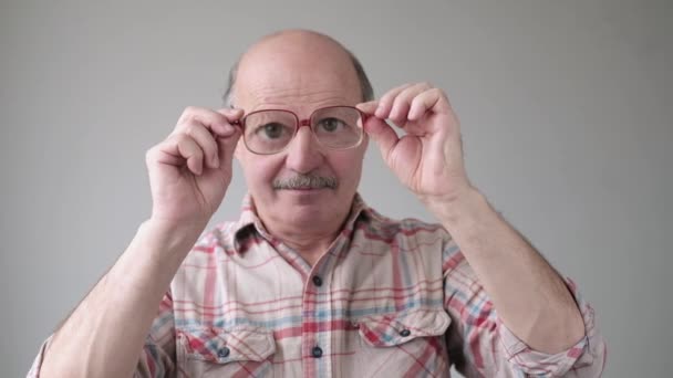 Förvånad stilig senior man tittar igenom glasögon på chockinnehåll. — Stockvideo