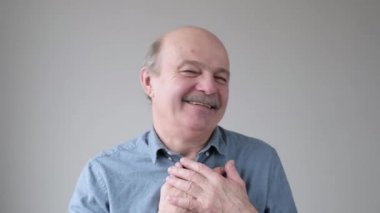 Neşeli kıdemli İspanyol adam mutlu bir şekilde gülümser, ellerini göğsüne koyar, olumlu duygularını ifade eder..