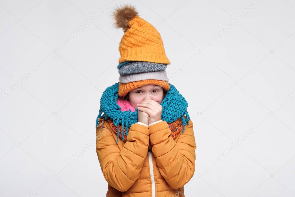 Funny young caucasian woman shivering from cold wearing several warm winter hats and scarfs