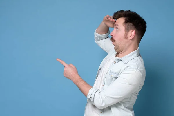 Joven señalando, sorprendido por algo o alguien, aislado sobre fondo azul . —  Fotos de Stock