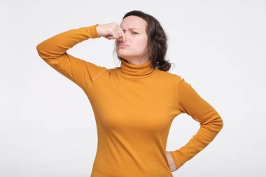 Genç beyaz kadın kötü bir koku yüzünden burnunu tutuyor.