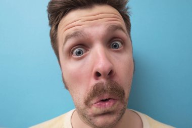 Şaşırmış genç adam portresi mavi arka planda izole edilmiş.