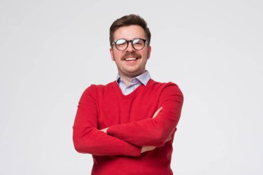 Kırmızı kazaklı ve gözlüklü bir adam kameranın önünde duruyor, pozitif ve kendinden emin hissediyor.