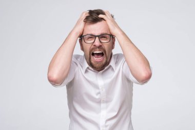 Gözlüklü genç adam umutsuz ve sinirli görünüyor, stresli, mutsuz ve sinirli, bağırıyor ve çığlık atıyor.