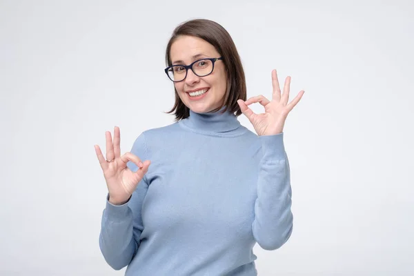 Caucásico madura mujer con amplia sonrisa usando gafas mostrando ok símbolo con los dedos . — Foto de Stock