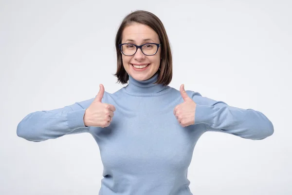 Молода випадкова жінка в окулярах в блакитному одязі ізольована на білому тлі, показуючи великі пальці вгору — стокове фото