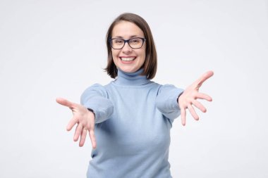 Gözlüklü kadın sana sarılmak için ellerini yana açıp gülümseyerek sarılıyor.