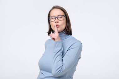 Bayan iş arkadaşı, gizli bilgileri gizli tutmak istiyor. Mavi gömlekli, beyaz stüdyo duvarına karşı duruyor..