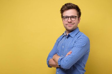 Sarı arka plana gülümseyen, katlanmış elleri olan yakışıklı bir genç.