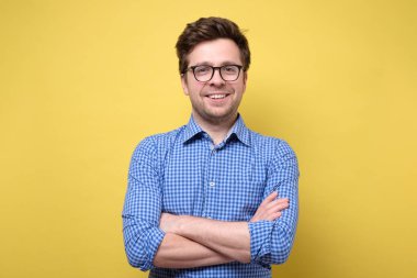 Sarı arka plana gülümseyen, katlanmış elleri olan yakışıklı bir genç.