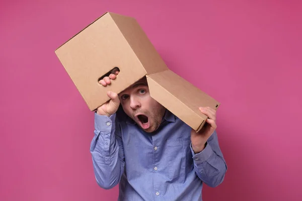 Muž v modré košili s hnědou papírovou krabicí na hlavě, skrývající se před pracovním stresem. — Stock fotografie