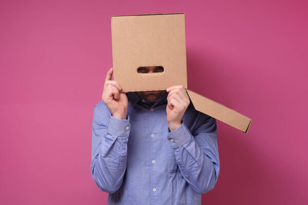 Man in blue shirt with a brown paper box on his head, hiding from job stress.