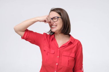 Mature caucasian man in glasses and red shirt plugs close nose with fingers feels unpleasant scent clipart