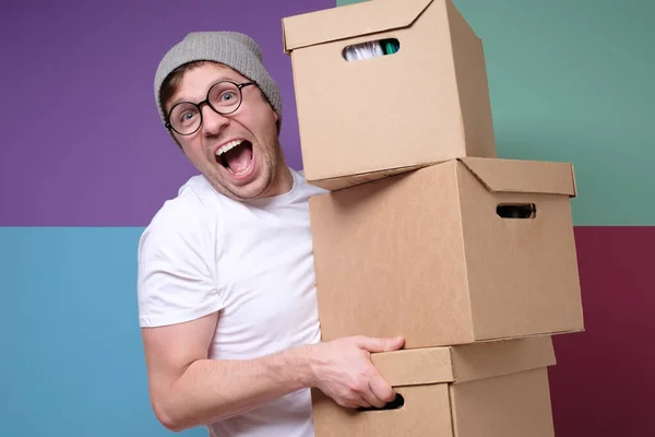 帽子と眼鏡の若いヒップスター男は、色の背景に隔離された紙箱を運ぶ — ストック写真