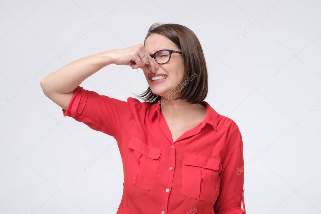 Mature caucasian man in glasses and red shirt plugs close nose with fingers feels unpleasant scent