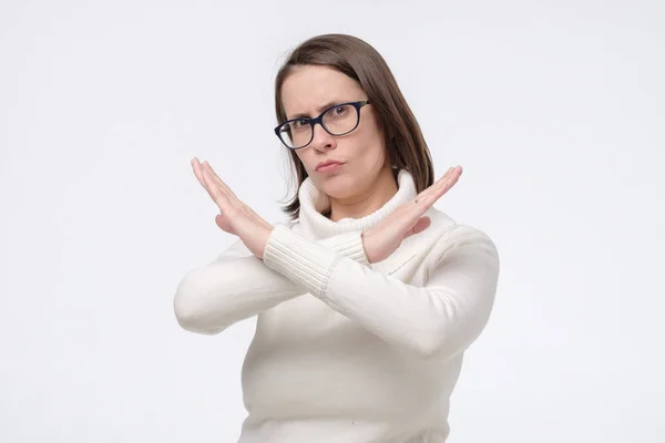 Mujer madura seria en gafas y suéter blanco haciendo señal de stop sobre fondo blanco . — Foto de Stock