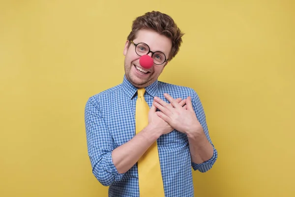 Clown allegro uomo con il naso rosso sorride felicemente, tiene le mani sul petto, esprime la sua emozione positiva — Foto Stock