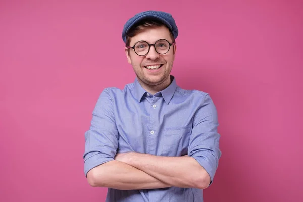 Homem caucasiano feliz em óculos e chapéu com as mãos dobradas no fundo rosa . — Fotografia de Stock