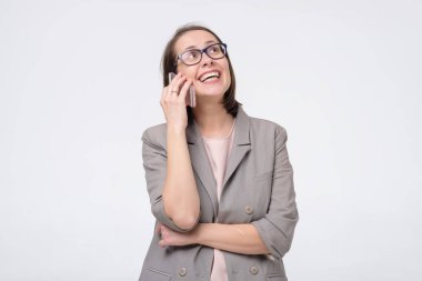 Gözlüklü ve takım elbiseli bir iş kadını telefonda konuşuyor.