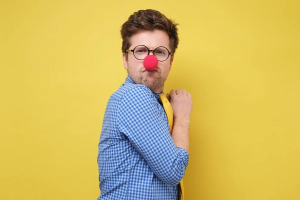 Un giovane avido con il naso rosso da clown nasconde qualcosa nelle sue mani e guarda cautamente avanti — Foto Stock