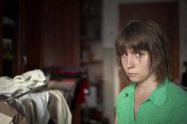 Genç beyaz kadın bir odada bir yatakta oturuyor..