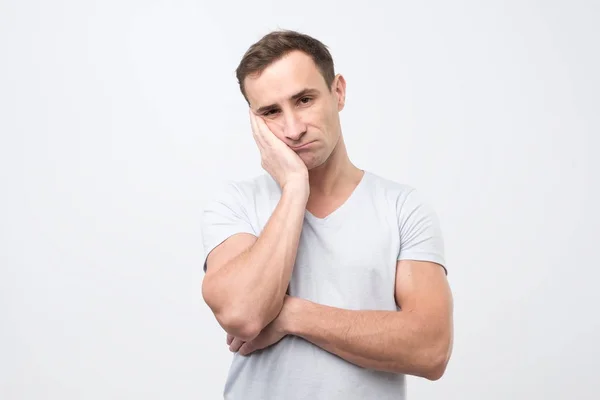 Hombre adulto cogido de la mano en la mejilla buscando cansado y enfermo, sobre fondo gris después de un duro día de trabajo . — Foto de Stock