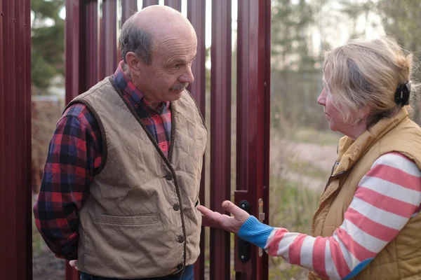 Rentnerin spricht in der Nähe von Zaun mit einem älteren Mann. — Stockfoto