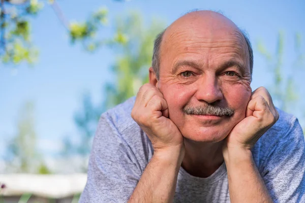 Eldre, spansktalende mann som hviler på frisk luft på bakken og smiler til kameraet . – stockfoto