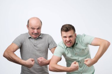 Two mature strong men, raising clenched fists showing their power being joyful and thrilled.