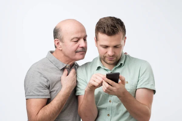 Father looking on his son mobile phone screen trying to understand how to use app. — 스톡 사진