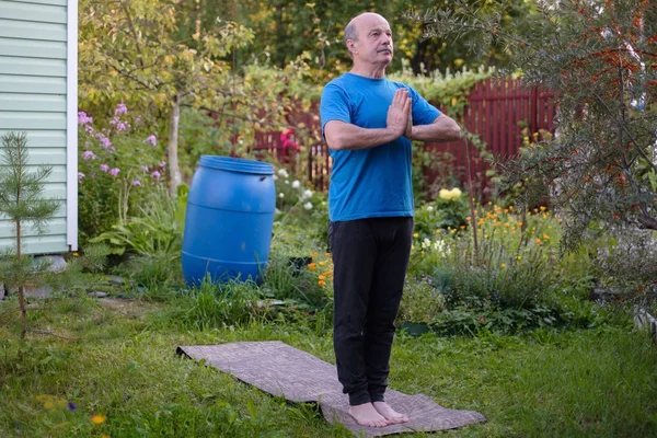 Homem sênior praticando ioga de pé em tadasana em seu jardim . — Fotografia de Stock