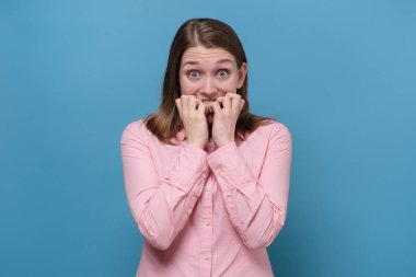 woman biting gnawing fingers, looking in camera with scared expression