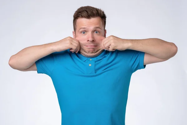 Uomo caucasico in t-shirt blu che si estende la pelle sul viso . — Foto Stock