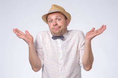 Clueless, funny looking young man in summer hat holding arms out asking what is problem