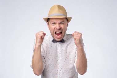 Kızgın, şapkalı, kelebek kravatlı, yumrukları havada bağıran genç bir adam.