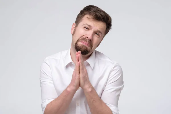 Emotive guy clenching hands together frowning while begging for forgiveness — Stock Photo, Image