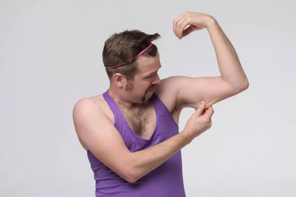 Deportista débil divertido haciendo ejercicio mirando sus bíceps . — Foto de Stock