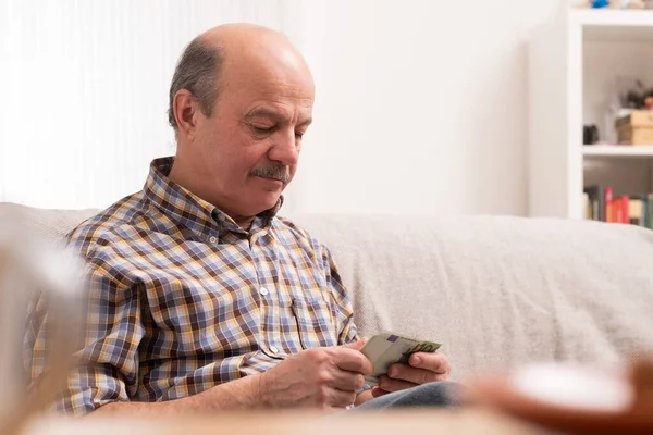 Senior man upptagen med att räkna pengar och räkningar hemma, sitter ensam hemma. — Stockfoto