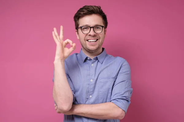 Pria Muda Tersenyum Dengan Kacamata Tersenyum Menunjukkan Simbol Terisolasi Dinding — Stok Foto