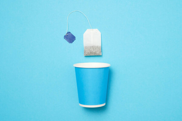 Blue paper cup with tea bag on blue wall. Top view