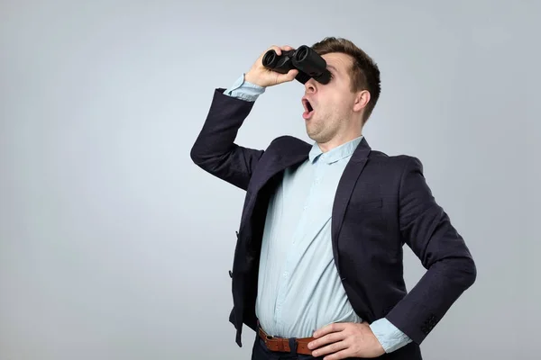 Young shocked businessman looking to the future through binoculars against a white background