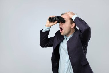 Genç şaşkın işadamı beyaz bir arka planda dürbünle geleceğe bakıyor.