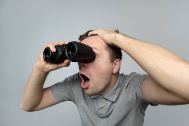 Genç şok olmuş bir adam beyaz bir arka planda dürbünle geleceğe bakıyor