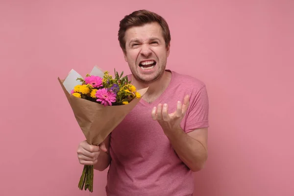 Amant en colère ou homme au cœur brisé en vêtements roses debout avec bouquet de fleurs . — Photo