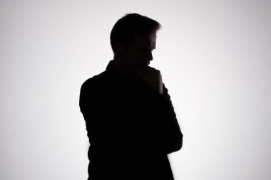 Gri stüdyo duvarında sorun ya da sorun hakkında düşünen bir adam silueti.